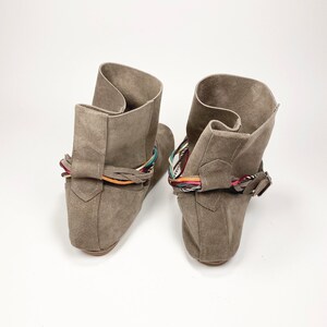 May include: A pair of gray suede ankle boots with colorful braided straps around the ankle.