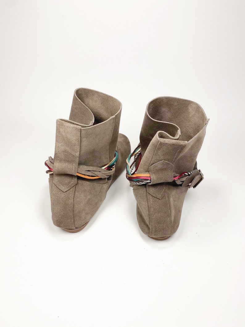 May include: A pair of gray suede ankle boots with colorful braided straps around the ankle.