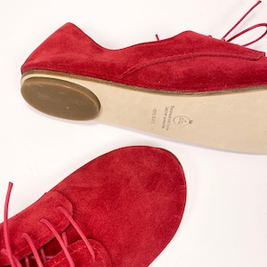 May include: Red suede lace-up shoes with a brown rubber sole. The shoes have a white leather label on the sole that reads "Limited edition Leather handmade 15/200".