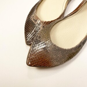 Peut inclure: Une paire de ballerines &agrave; bout pointu avec un motif peau de serpent dans les tons marron, gris et beige. Les chaussures ont un petit talon et un int&eacute;rieur de couleur neutre. Les ballerines sont probablement en cuir ou dans une mati&egrave;re similaire.