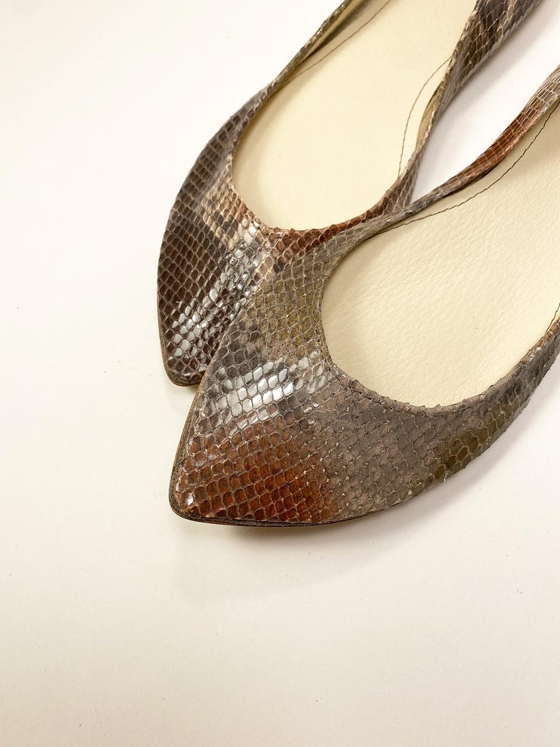 Peut inclure: Une paire de ballerines &agrave; bout pointu avec un motif peau de serpent dans les tons marron, gris et beige. Les chaussures ont un petit talon et un int&eacute;rieur de couleur neutre. Les ballerines sont probablement en cuir ou dans une mati&egrave;re similaire.