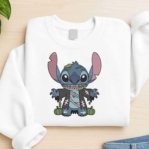 May include: White sweatshirt featuring a cartoon zombie Stitch character with blue skin, large ears, and green slime. The design includes pumpkins and stitched details, perfect for Halloween.