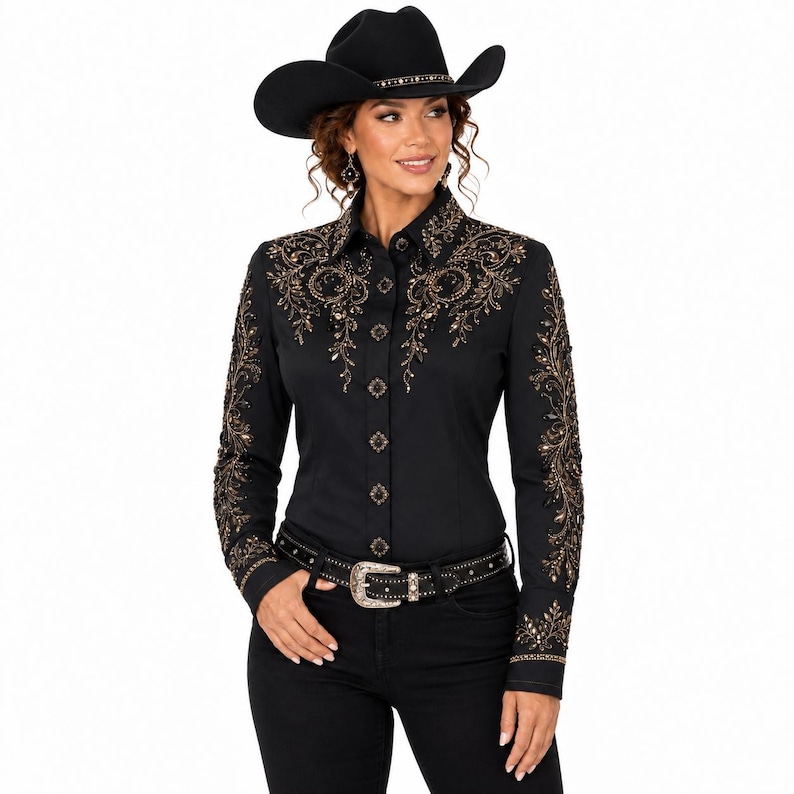 Puede incluir: Una camisa negra de manga larga con botones y bordados florales en tonos oro y bronce en hombros y mangas, acompa&ntilde;ada de un sombrero de vaquero negro y un cintur&oacute;n negro con hebilla plateada, sobre pantalones de color negro.
