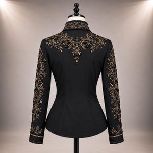 Puede incluir: Una chaqueta negra de manga larga con intrincados bordados en dorado y bronce en los hombros, el cuello y a lo largo de cada manga. El dise&ntilde;o incluye patrones florales ornamentados y adornos oscuros en los pu&ntilde;os y la parte posterior.