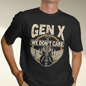 Op de afbeelding: Een zwart t-shirt met korte mouwen en een grafische print met de tekst "GEN X WE DON'T CARE" in een verweerd lettertype. Het ontwerp bevat een centrale elektrische gitaar met vleugels, vlammen en een cirkelvormige regenboogkleurige rand.