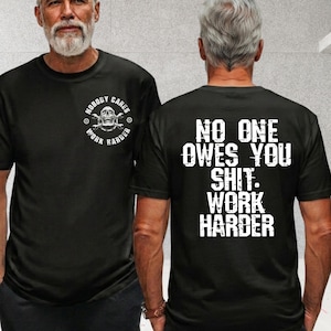 Könnte beinhalten: Ein schwarzes Kurzarm-T-Shirt mit einer weißen Grafik auf der Brust, die einen Totenkopf mit gekreuzten Schraubenschlüsseln und den Text "NOBODY CARES WORK HARDER" zeigt. Auf der Rückseite steht der weiße Text "NO ONE OWES YOU SHIT. WORK HARDER".