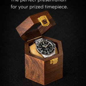 Peut inclure: Coffret à montre en bois foncé avec couvercle à charnière, présentant une montre à cadran noir et bracelet argenté. Le coffret a des fermoirs dorés et un intérieur beige. Le texte dit: 'ELEGANT WOODEN WATCH BOX'.