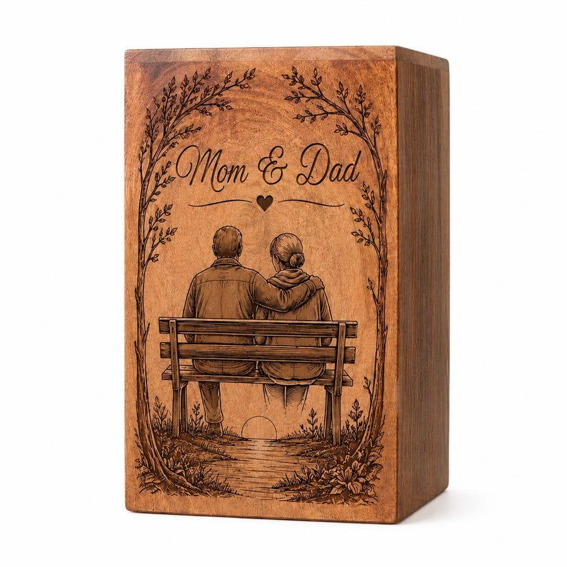 Pu&ograve; includere: Un'urna rettangolare in legno con un'illustrazione incisa al laser di due persone sedute su una panchina sotto degli alberi. Il testo Mom & Dad &egrave; centrato sopra le figure con un piccolo cuore. La scena include un sentiero e un sole.