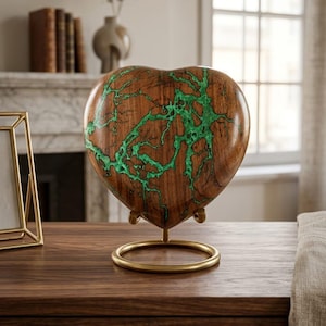 Könnte beinhalten: Eine herzförmige Holzskulptur mit grüner Maserung, präsentiert auf einem goldfarbenen Metallständer. Die Skulptur besteht aus braunem Holz und hat eine glatte, polierte Oberfläche. Der Ständer hat einen kreisförmigen Sockel und einen einzelnen Stiel.