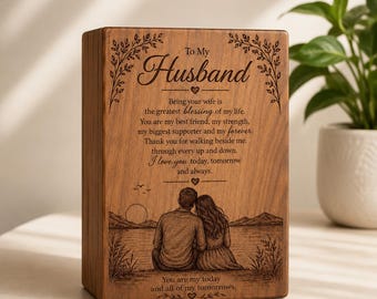 Può includere: Una scatola rettangolare in legno con testo inciso al laser che recita To My Husband, seguito da un messaggio sentimentale e un'illustrazione di una coppia seduta vicino a un lago. Include bordi decorativi a foglia e cuori.