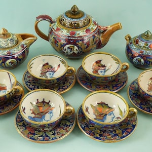 May include: A complete antique tea set with a teapot, creamer, sugar bowl, and six teacups with saucers. The set features a colorful, ornate design with blue, red, and gold accents. The teacups and saucers have a portrait of a person.