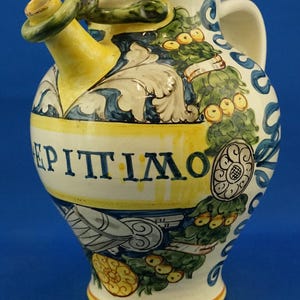 May include: A ceramic pitcher with a yellow spout and handle, decorated with blue and green floral patterns and the word "EPITIMO" in black. The pitcher has a white base and a blue background.