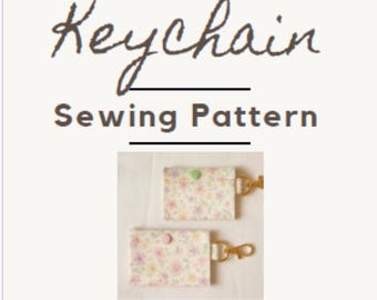 May include: A sewing pattern for a wallet keychain. The image shows two finished keychains with floral fabric, snap closures, and gold-colored hardware. The text at the top reads "Wallet Keychain Sewing Pattern."