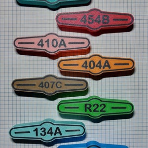 May include: A collection of colorful, oblong-shaped tags with rounded ends, each bearing a unique alphanumeric code in black. The tags are in various colors, including teal, pink, orange, brown, green, light blue, and dark blue.