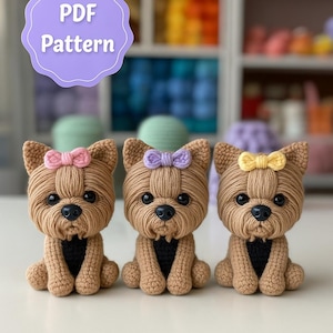 Könnte beinhalten: Drei gehäkelte Yorkshire Terrier Hundefiguren mit braunen Garnkörpern, schwarzen Nasen und Augen. Jeder Hund hat eine andersfarbige Schleife: rosa, lila und gelb. Das Bild enthält den Text "PDF Pattern" in einer lila Blase.