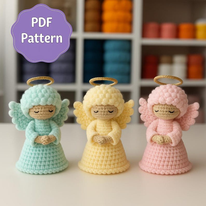 May include: Three crocheted angel figurines in pastel colors: light blue, yellow, and pink. Each angel has a halo, wings, and closed eyes, with hands clasped in prayer. The image includes a purple circle with the text "PDF Pattern".