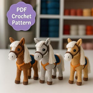 May include: Three crocheted toy horses in shades of brown, gray, and yellow, each with a white mane and tail, and a blue and orange saddle. The image includes a purple sign that says "PDF Crochet Pattern".