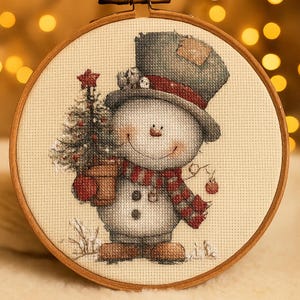 May include: A cross-stitch embroidery of a snowman holding a Christmas tree in a wooden hoop. The snowman wears a gray hat, red scarf, and mittens. The tree has a red star on top and is in a brown pot. A red ornament hangs from the snowman's scarf.