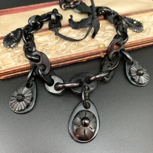 May include: A vintage black necklace with a chain-link design and decorative floral pendants. The necklace features a black ribbon tie closure and is displayed against a neutral background. The pendants have a detailed, carved appearance.