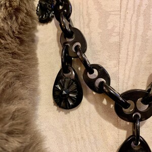 May include: Close-up of a black chain necklace with teardrop-shaped pendants. The pendants have a starburst design. The chain links are oval and connected by smaller, curved links. The necklace is set against a neutral background.