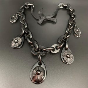 May include: A silver-toned chain bracelet with multiple teardrop-shaped charms and flower-like pendants. The bracelet has a chunky chain design and a bow-shaped clasp. The charms and pendants add a decorative element to the jewelry.