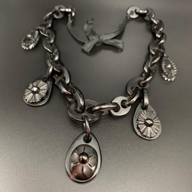 May include: A silver-toned chain bracelet with multiple teardrop-shaped charms and flower-like pendants. The bracelet has a chunky chain design and a bow-shaped clasp. The charms and pendants add a decorative element to the jewelry.