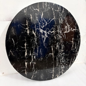 May include: A round, black marble tabletop with white veining. The polished surface reflects light, highlighting the intricate patterns. This decorative piece is suitable for various home decor styles.