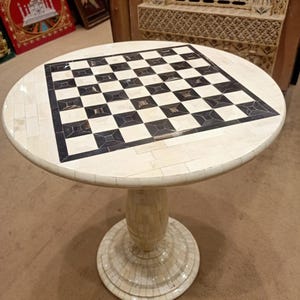Peut inclure: Une table de jeu d'échecs ronde avec une base et un plateau de couleur crème. Le plateau présente un motif à carreaux noir et blanc. La table mesure environ 71 cm de diamètre et 74 cm de haut, une pièce décorative pour les amateurs de jeux.