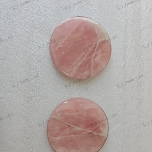 Op de afbeelding: Twee ronde onderzetters van gepolijst rozenkwarts. De onderzetters hebben een zachtroze kleur met natuurlijke adering. Ze zijn glad en lijken van massief steen te zijn gemaakt. Ontworpen voor gebruik met dranken.