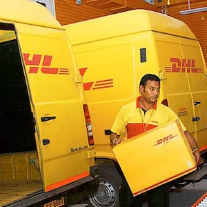 May include: A yellow DHL delivery van with the door open, and a man in a yellow and red shirt carrying a yellow box with the DHL logo. The van has the DHL logo on the side.