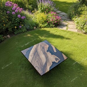 May include: A square coffee table with a dark blue resin center and a natural wood grain border. The table is set on a green lawn, surrounded by a garden with flowers and greenery.