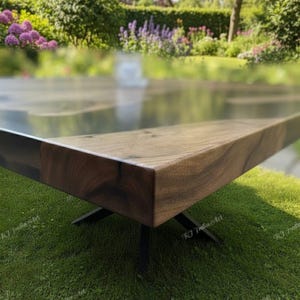 May include: A modern wooden table with a dark finish and a sleek, rectangular design. The table has a natural wood grain and is supported by black metal legs. The table is set on a green lawn with a blurred garden background.