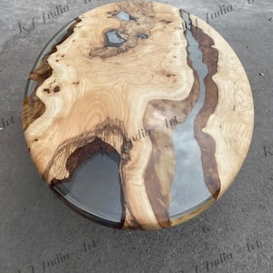 May include: A round wooden coffee table with a natural wood grain pattern and a clear epoxy resin river. The table is approximately 36 inches in diameter.