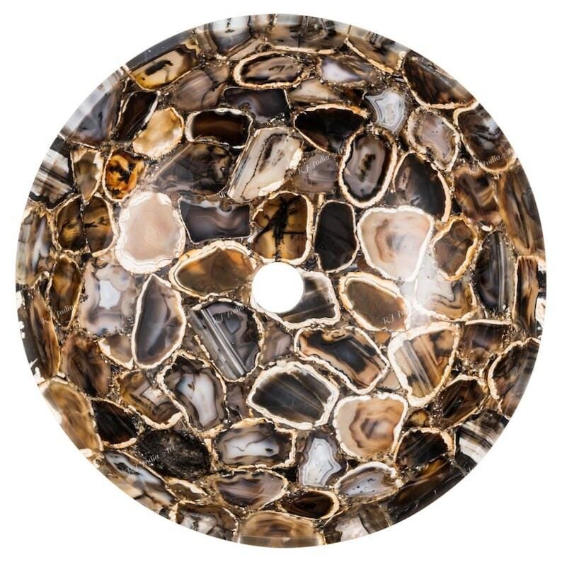 May include: A round, natural stone sink basin. The basin is composed of irregularly shaped, polished agate pieces in shades of brown, gray, and cream, with gold-colored edges. A circular drain hole is centered in the basin.