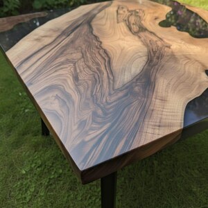 May include: Square wooden coffee table with a natural wood grain surface and dark epoxy resin accents. The table has a dark brown border and black metal legs. The table is approximately 36 inches wide and 36 inches long.