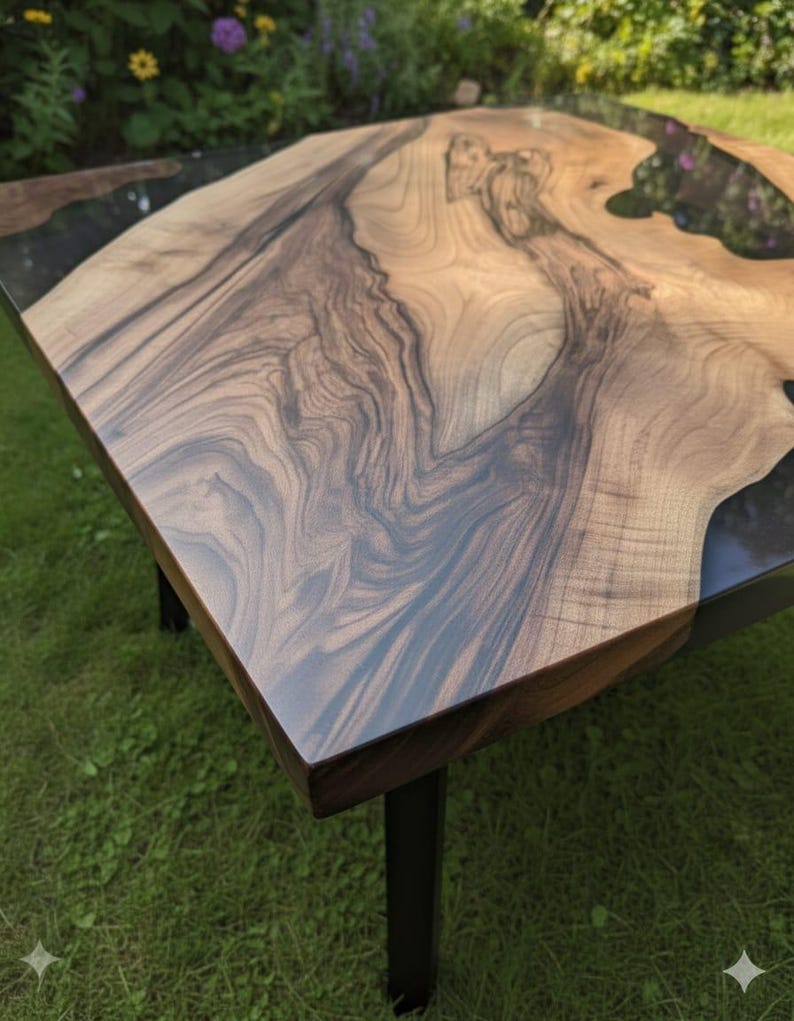 May include: Square wooden coffee table with a natural wood grain surface and dark epoxy resin accents. The table has a dark brown border and black metal legs. The table is approximately 36 inches wide and 36 inches long.