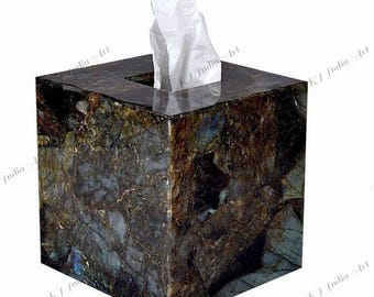 May include: A square tissue box made of dark, patterned stone. The box has a polished finish and a rectangular opening at the top, with white tissues partially visible. The stone features a mix of brown, blue, and gray tones.