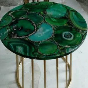 Puede incluir: Una mesa auxiliar redonda con una tapa hecha de rodajas de &aacute;gata verde. El &aacute;gata es una mezcla de tonos verdes oscuros y claros con detalles blancos y marrones. La mesa tiene una base de metal dorado.