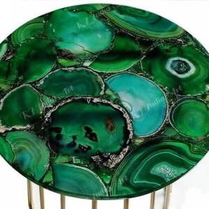 Puede incluir: Una mesa redonda con una vibrante tapa de piedra de &aacute;gata verde. La superficie est&aacute; compuesta por piezas irregulares de piedra verde pulida con diferentes tonos y patrones. La mesa tiene una base de metal color dorado.
