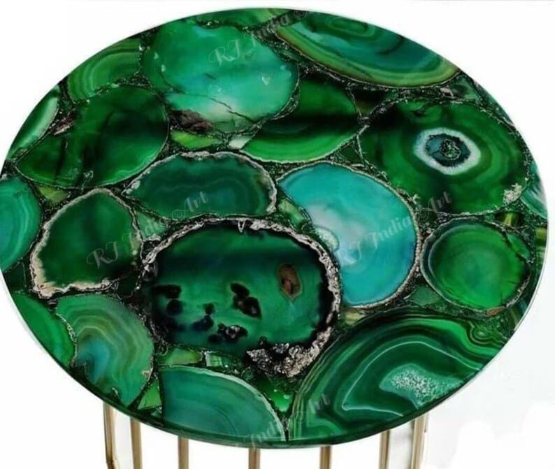 Puede incluir: Una mesa redonda con una vibrante tapa de piedra de &aacute;gata verde. La superficie est&aacute; compuesta por piezas irregulares de piedra verde pulida con diferentes tonos y patrones. La mesa tiene una base de metal color dorado.