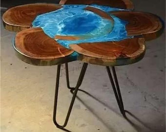 May include: A unique, handcrafted side table with a flower-like design. The table features a wooden top with a blue resin center, supported by black metal hairpin legs. The wood has a natural grain, and the resin mimics water.