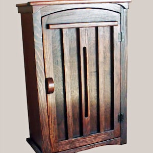 May include: A dark stained wooden cabinet with a single door. The door features vertical slats and a curved top. A small, rounded handle is on the left side. The cabinet is designed with a base and a top, showcasing a classic, handcrafted style.