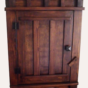 May include: A dark brown wooden cabinet with a single door and a simple design. The cabinet has a slightly arched base and a decorative top.