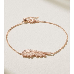 Op de afbeelding: Roségouden armband met een delicate vleugelvormige hanger, versierd met kleine, sprankelende kristallen. De armband heeft een ketting met een verstelbare sluiting. Een prachtig sieraad.