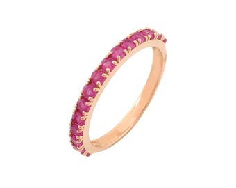May include: A rose gold ring with a band of vibrant pink gemstones. The ring features a continuous row of evenly spaced, round-cut stones, creating a full eternity band design. The ring's warm metal tone complements the bright pink of the gemstones.