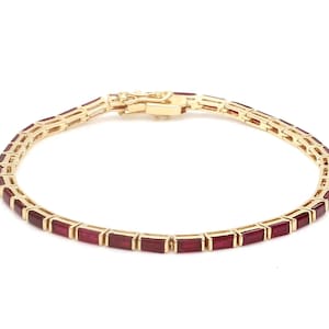 May include: A gold bracelet featuring a series of rectangular, deep red gemstones. The bracelet has a delicate design with a secure clasp. The gemstones are set in a gold band, creating a luxurious and elegant look.