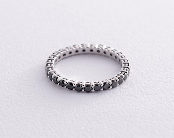 May include: A silver ring featuring a full band of small, round black gemstones. The ring is set against a plain white backdrop, accentuating the contrast between the polished metal and the dark stones. The ring is a classic eternity band design.