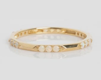 May include: A gold band ring with small, round, white gemstones set around the band. The ring has a polished finish and is set against a white background. The gemstones are evenly spaced around the ring.