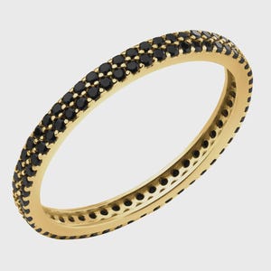 Könnte beinhalten: Ein goldfarbener Ring mit zwei Reihen kleiner, schwarzer Edelsteine. Der Ring hat ein schlichtes Banddesign, wobei die Edelsteine eng um den gesamten Umfang angeordnet sind. Der Ring wird vor einem schlichten, hellen Hintergrund gezeigt. Der Ring hat einen Durchmesser von ca. 1,7 cm.