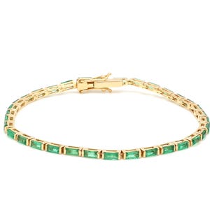 May include: A gold bracelet with rectangular emerald-green gemstones. The bracelet has a delicate design and a secure clasp. The gemstones are set in a row, creating a continuous line of colour. This piece of jewellery is suitable for various occasions.